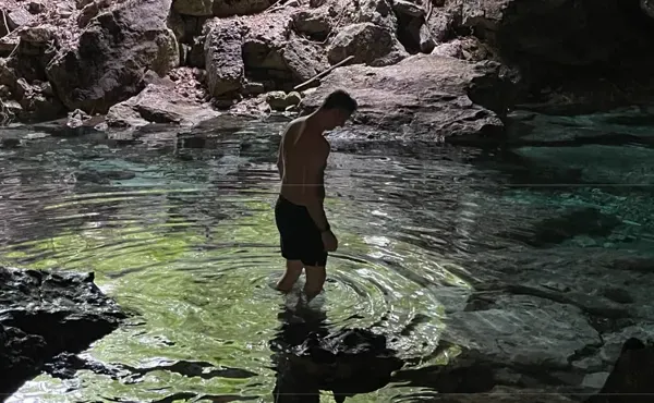 A person standing in a cenote, ripples spreading across the green water
