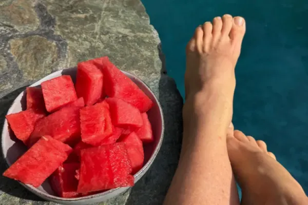 A bowl of sliced watermelon on the pool edge beside a pair of feet resting after a swim at Alma Chakana