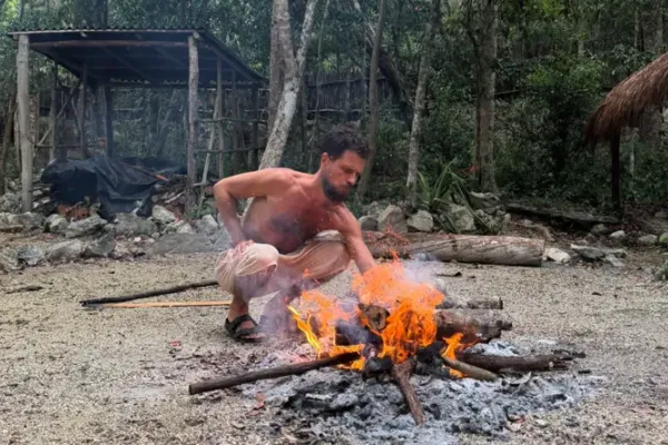 A man tending a fire outdoors at the jungle sanctuary, surrounded by trees and rocks