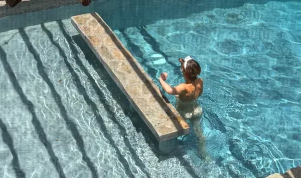 A person in the pool at Alma Chakana leaning on the stone steps beneath the wooden pergola