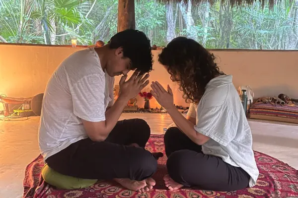 Two people sitting face to face in the practice space at Alma Chakana, hands meeting between them