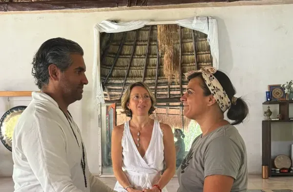 Three people in conversation in the retreat space at Alma Chakana, thatched roof behind them