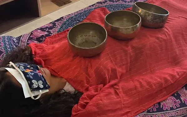A person lying under a red cloth with singing bowls resting on them during a sound session