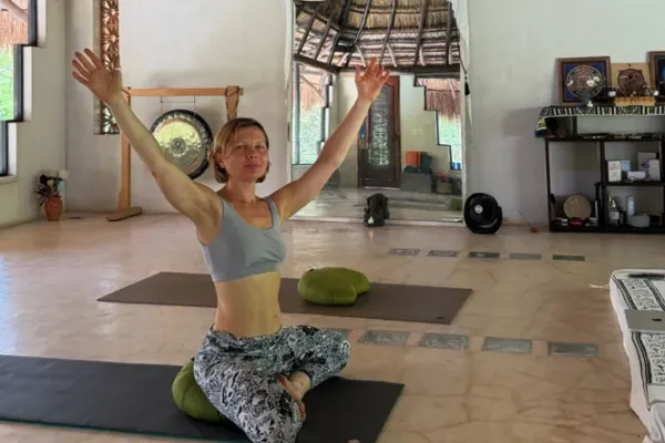 A guest practising yoga with arms raised in the practice space at Alma Chakana, gong behind her