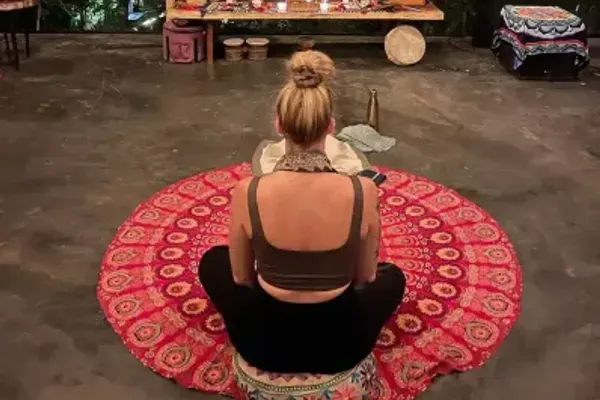 A guest sitting cross-legged on a round patterned rug facing an altar in the practice space at Alma Chakana