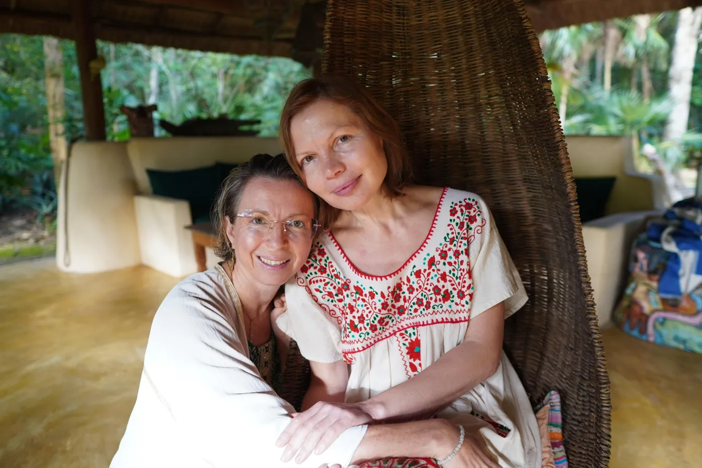 Lena and Olga, the facilitators of Compassion Retreats, sharing a moment in a hanging wicker chair under a thatched jungle pavilion
