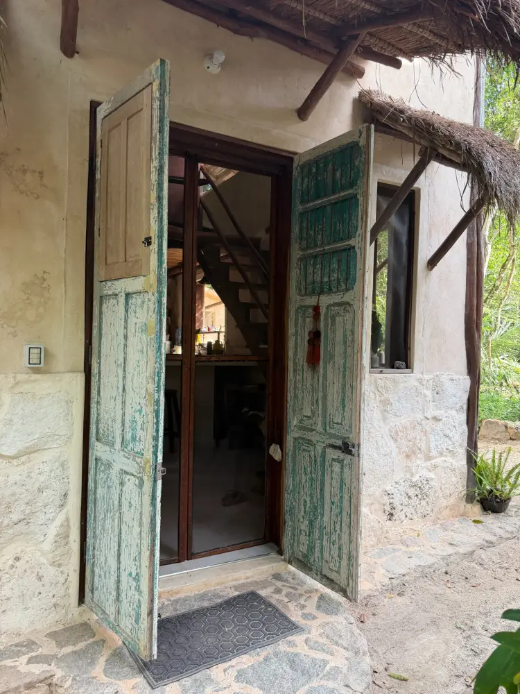 The rustic entrance to our jungle sanctuary, with weathered green doors beneath a thatched roof